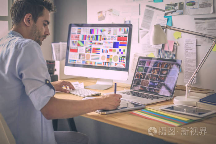 年轻设计师的肖像坐在平面工作室前的笔记本电脑和电脑, 而在线工作