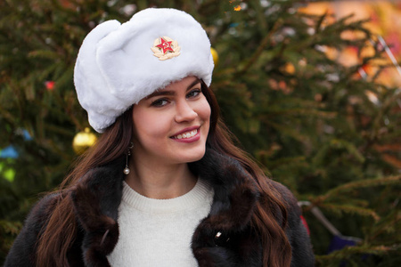 俄罗斯美女。莫斯科一个年轻漂亮的女孩戴着一顶带毛皮帽子的白帽子对着一个红色广场的画像