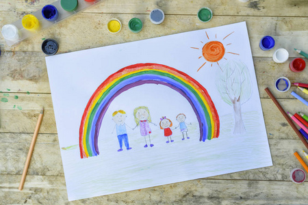 幸福的家庭观念。 画木桌爸爸妈妈男孩和女孩在彩虹和晴朗的天空的背景下牵手