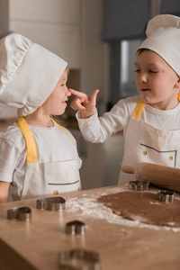 戴着帽子和围裙的快乐孩子烤饼干。 厨房。 家庭概念