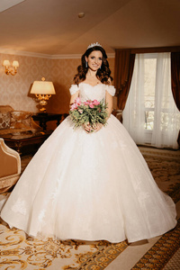 时尚内饰照片美丽的女人新娘，黑发，豪华婚纱，手捧鲜花摆在优雅的房间里