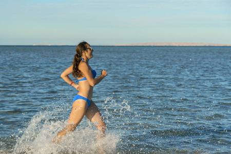 的年轻黑发女人穿着比基尼在荒凉的热带海滩上冲浪，蓝天。