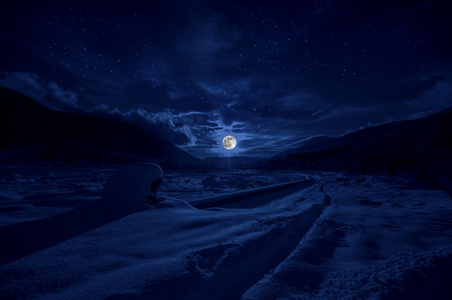 雄伟的冬夜在一个山谷里,满月在星空中. 有月亮的美丽的雪夜景观照片