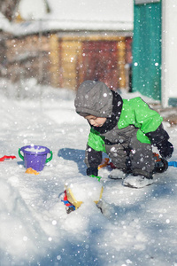 可爱的小蹒跚学步的孩子坐在雪地上，在公园里玩他的黄色拖拉机玩具的肖像。 孩子们在户外玩耍。 带建筑玩具的快乐男孩。 生活方式的概