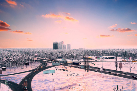 冬季城市全景与道路和交通附近的森林日落。 水平视图
