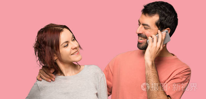 情人节那天,一对夫妇在孤立的粉红色背景下与手机交谈照片-正版商用