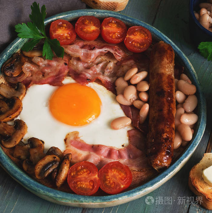 传统的英国早餐炒鸡蛋,培根,蘑菇,香肠,豆类和樱桃西红柿,在一个乡村