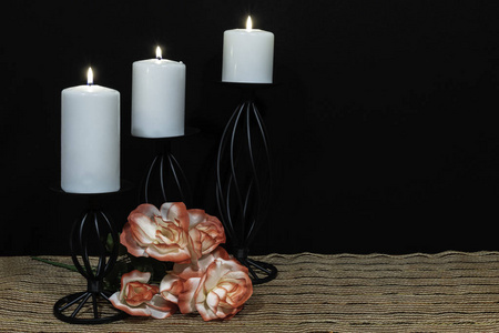 美丽的橙色和白色玫瑰，白色蜡烛栖息在黑色烛台上，在网状的地方，垫子和木制的桌子，黑色的背景。 情人节母亲节复活节圣诞节婚礼概念