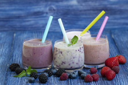 覆盆子，草莓，黑莓，蓝莓，冰沙，蓝色木制背景。 带新鲜浆果的奶昔。 健康的早餐。 水果奶昔和配料。 福利和重量宽松的概念