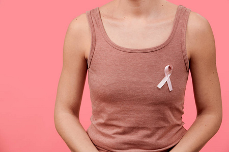 一名年轻女子的中段，身穿粉红色乳腺癌意识丝带，隔离在活的珊瑚背景上。 医疗保健人员慈善和医学概念。
