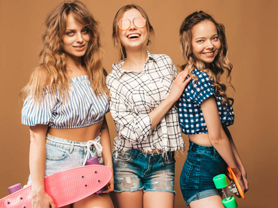 三个年轻时尚，，微笑，美丽的女孩，五颜六色的棋盘。夏天穿着时髦衬衫的女人戴着太阳镜，摆在金色墙壁附近。积极的模特玩得开心
