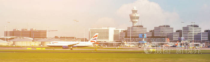 繁忙的机场景观与飞机和服务车辆在日落。 机场，飞机在大门和起飞卡车周围和日落背景。 旅行和工业概念