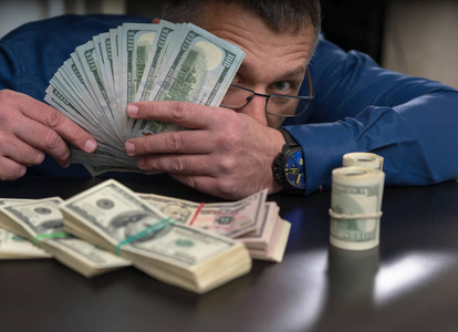 赌徒商人,赌徒或腐败的官员戴着眼镜,从一把钱后面看出来,面前有一捆