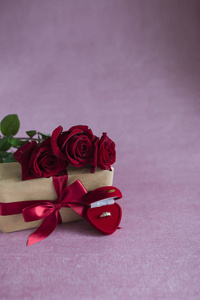 礼品盒上的红玫瑰粉红色背景上的戒指盒鲜花礼物和粉红色背景上的戒指结婚的建议垂直复制空间