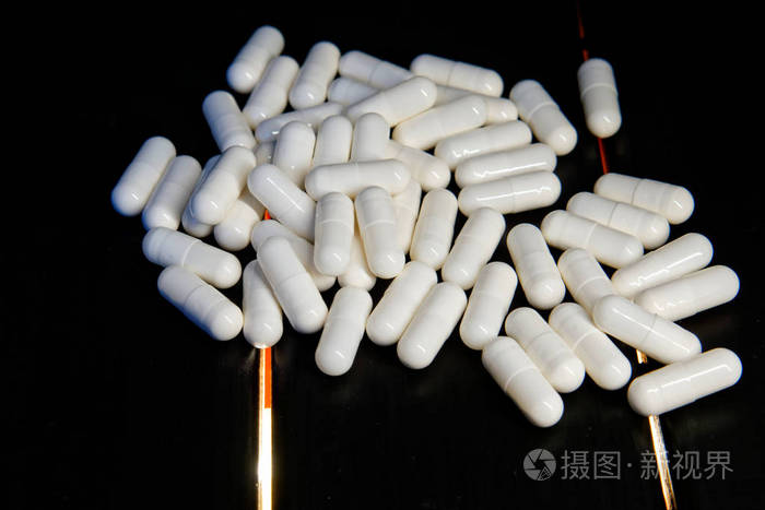 白色胶囊药丸在黑色木制背景与led灯. 医学和健康.
