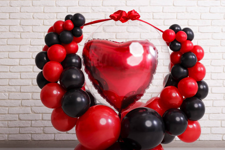 情人节的概念。 气球的设计是黑色的，中间有一颗大心脏。 绷带节日丝带。 在白色砖墙上