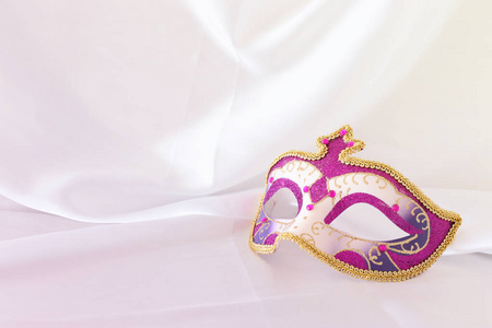 白色丝绸背景上优雅细腻的粉红色紫色和金色威尼斯面具的照片
