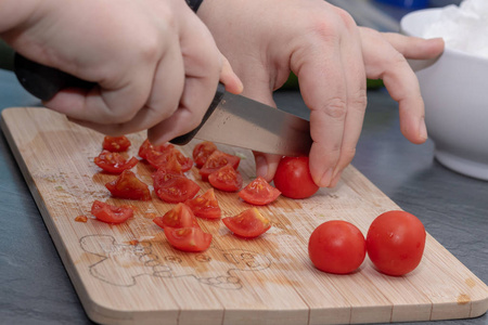 s hands cutting tomato, behind fresh vegetables.