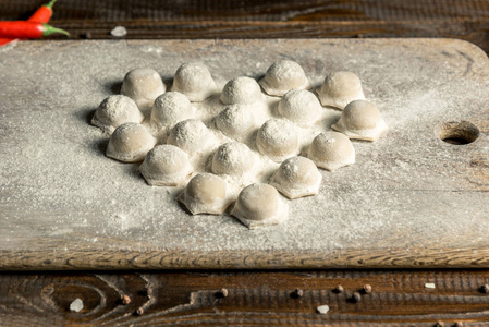 乌兹别克国民食品Chuchvara就像饺子一样，躺在面粉中的木板上，心形的。 水平框架