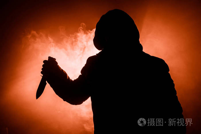 一个危险的蒙面人站在黑暗中拿着一把刀. 脸是看不见的. 实施犯罪概念