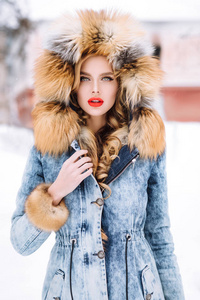 美丽的金发女孩在雪地里披着冬天的毛皮大衣