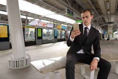 在火车站使用手机的年轻商人