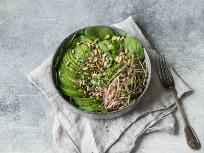 绿色健康沙拉菠菜芽菜鳄梨和各种种子放在蓝色的碗里