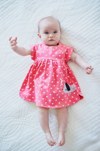六个月大的穿粉红色裙子的女婴。 穿着鲜艳衣服的小孩躺在托儿所的床上。 婴儿时尚