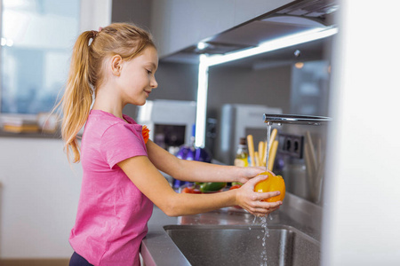长头发漂亮的女孩在厨房里洗蔬菜粉红色衬衫