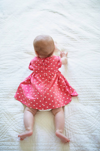 六个月大的穿着粉红色裙子的女婴试图爬行。 穿着鲜艳衣服的小孩躺在托儿所的床上。 婴儿时尚