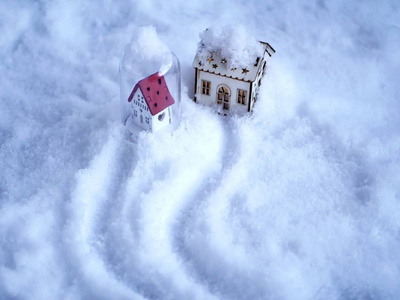 两个小玩具房子，雪上有灯光照明，雪上有小径，在房子里祝贺情人节，圣诞节，家庭，爱的概念