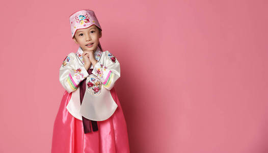 亚洲枕为祈祷韩国小女孩在传统丝绸礼服为新年庆祝在粉红色与手在祈祷