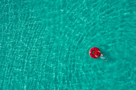 在塞舌尔透明的绿松石海中游泳圈上游泳的苗条女人的空中景色。夏日海景带少女，美丽海浪，缤纷水色..无人驾驶飞机的俯视图