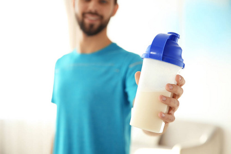 年轻的运动男子带着一瓶蛋白奶昔在家，特写