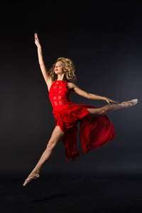 穿着红色裙子跳着芭蕾的漂亮年轻女孩在黑色背景下摆姿势