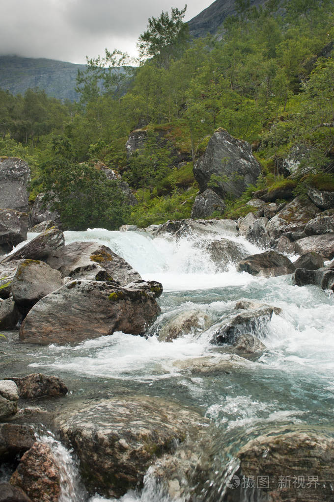挪威的一条多山的湍急的河流在绿色山坡背景下的巨石之间