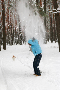 冬天的松林里，一个长着红胡子的开朗英俊的年轻人和一只狗的肖像。 在冬天的一天，他从松枝上吹雪。 高大的松树。 垂直定向