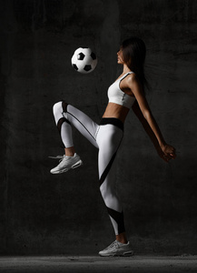 足球女子球员跳跃和击中球罢工在中间在混凝土阁楼墙上