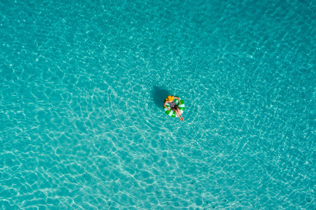 鸟瞰苗条的女人在塞舌尔透明的绿松石海中游泳圈甜甜圈。 夏天海景与女孩美丽的波浪，五颜六色的水。 无人驾驶飞机的俯视图