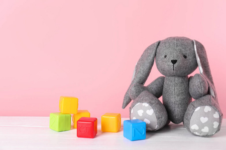 可爱的玩具兔子和塑料立方体在桌子上的颜色背景空间为文本。 儿童房间单元