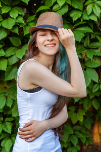 美丽的年轻时髦女孩，戴着帽子，长发，绿色的头发，在公园的背景上微笑。 欧洲女人。 酷炫时髦少女户外休闲画像