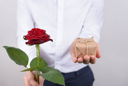 特写照片，英俊迷人快乐开朗积极向上的男人，手里拿着小礼物和明亮的玫瑰，孤立的灰色背景