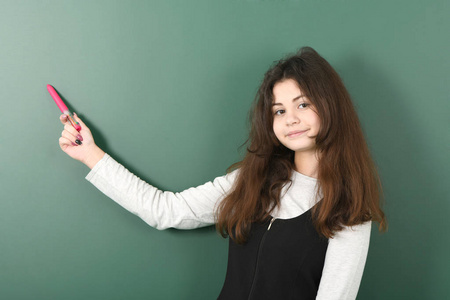 绿色背景上微笑的小女生。 年轻活泼的女孩手里拿着红笔