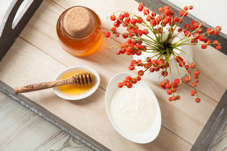 新鲜蜂蜜和天然牛奶酸奶，放在木制托盘上的白瓷餐具中，装饰着秋天的花束