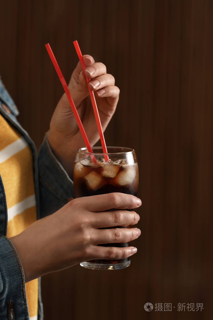 女人拿着一杯加冰的可乐在模糊的背景下特写