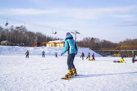 一个年轻的女孩穿着一套特殊的彩色西装，为冬季的乐趣和运动学习骑滑雪板在一个阳光明媚的日子。