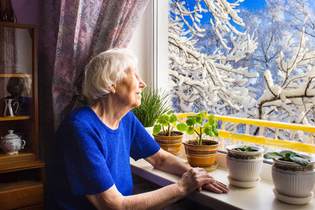 老孤独的女人坐在他的房子窗户附近
