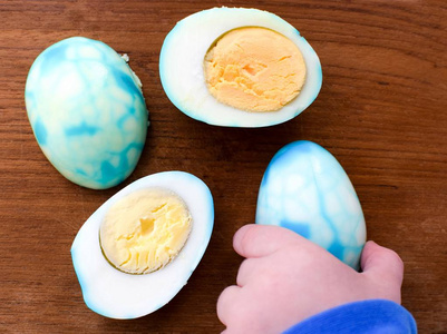 一支小孩子的钢笔拿着一个去皮的鸡蛋, 上面有蓝色和绿松石色的条纹, 被涂成复活节