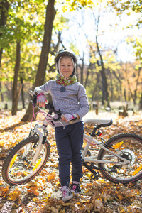 可爱的小女孩在秋天的森林里骑自行车。