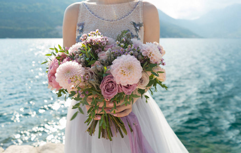 新娘在她的臂弯里抱着粉红色和淡紫色的婚礼花束, 在大海的背景下